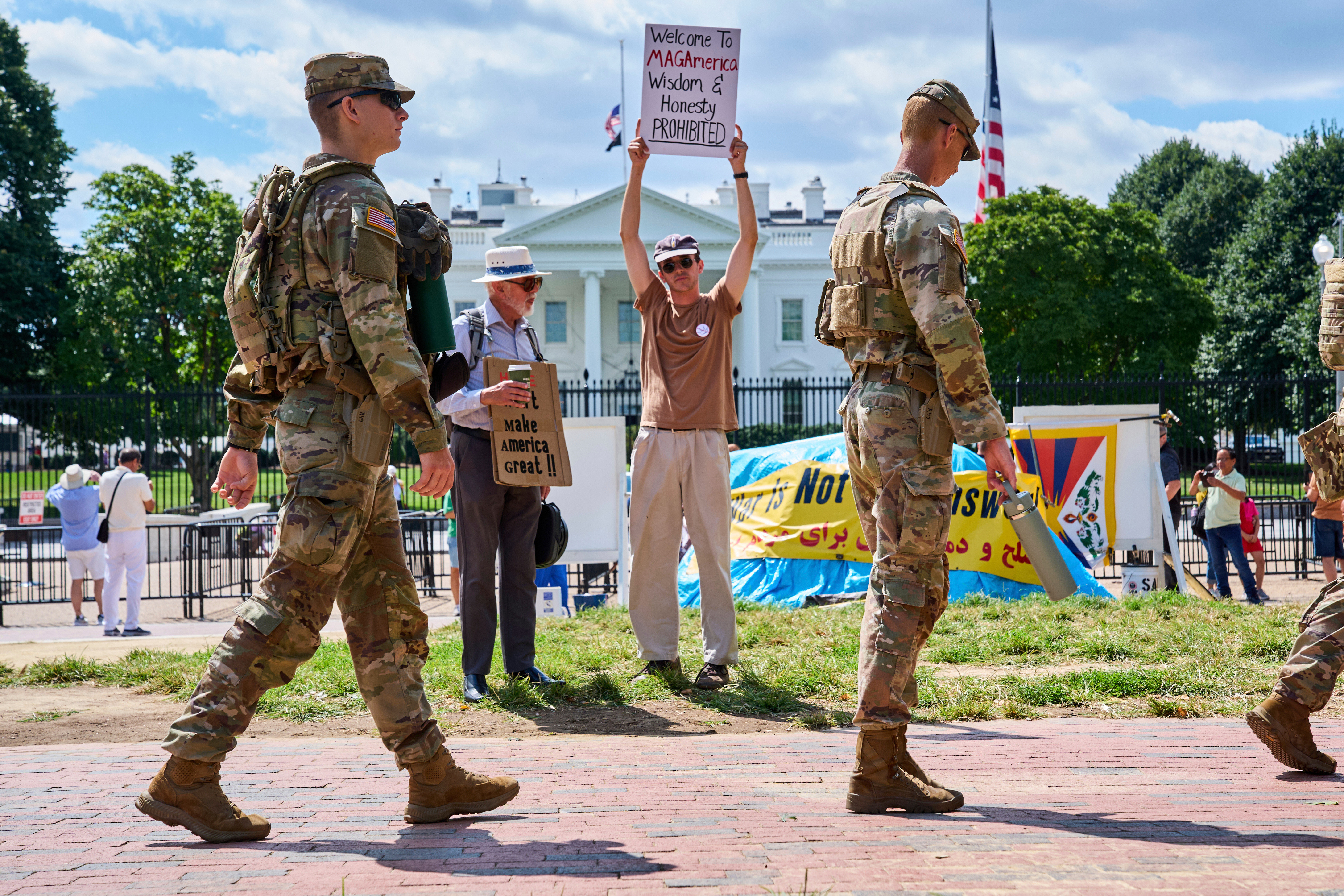 Members of the National Guard patrol Lafayette Park by the White House, Friday, Aug. 29, 2025, in Washington, while protester Will Roosien, of Grand Rapids, Mich., who says he hopes to inspire others of his generation to protest, holds up a sign about the MAGA movement. (AP Photo/Jacquelyn Martin)